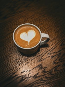 A warm latte with heart-shaped foam art on a textured wooden table, perfect for coffee lovers.