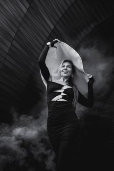 Stylish woman in black dress and large hat, captured in dramatic black and white photography.