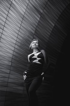 A stylish woman poses confidently in a modern architectural setting, black and white.