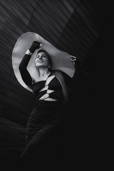 Elegant woman in fashion dress and hat posing outdoors in striking black and white.