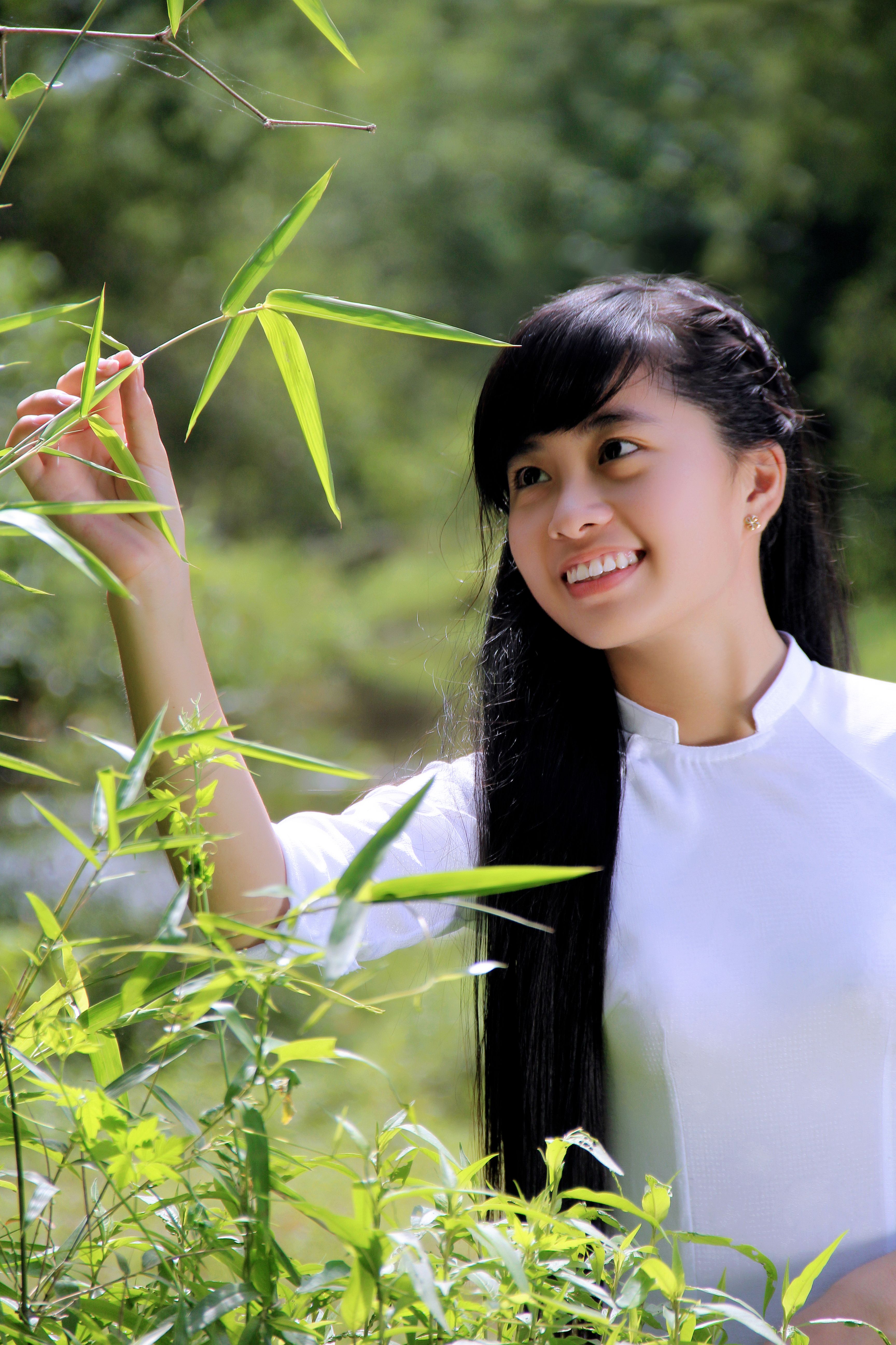 A smiling young woman in an Ao Dai admires bamboo greenery in Hội An, Vietnam.