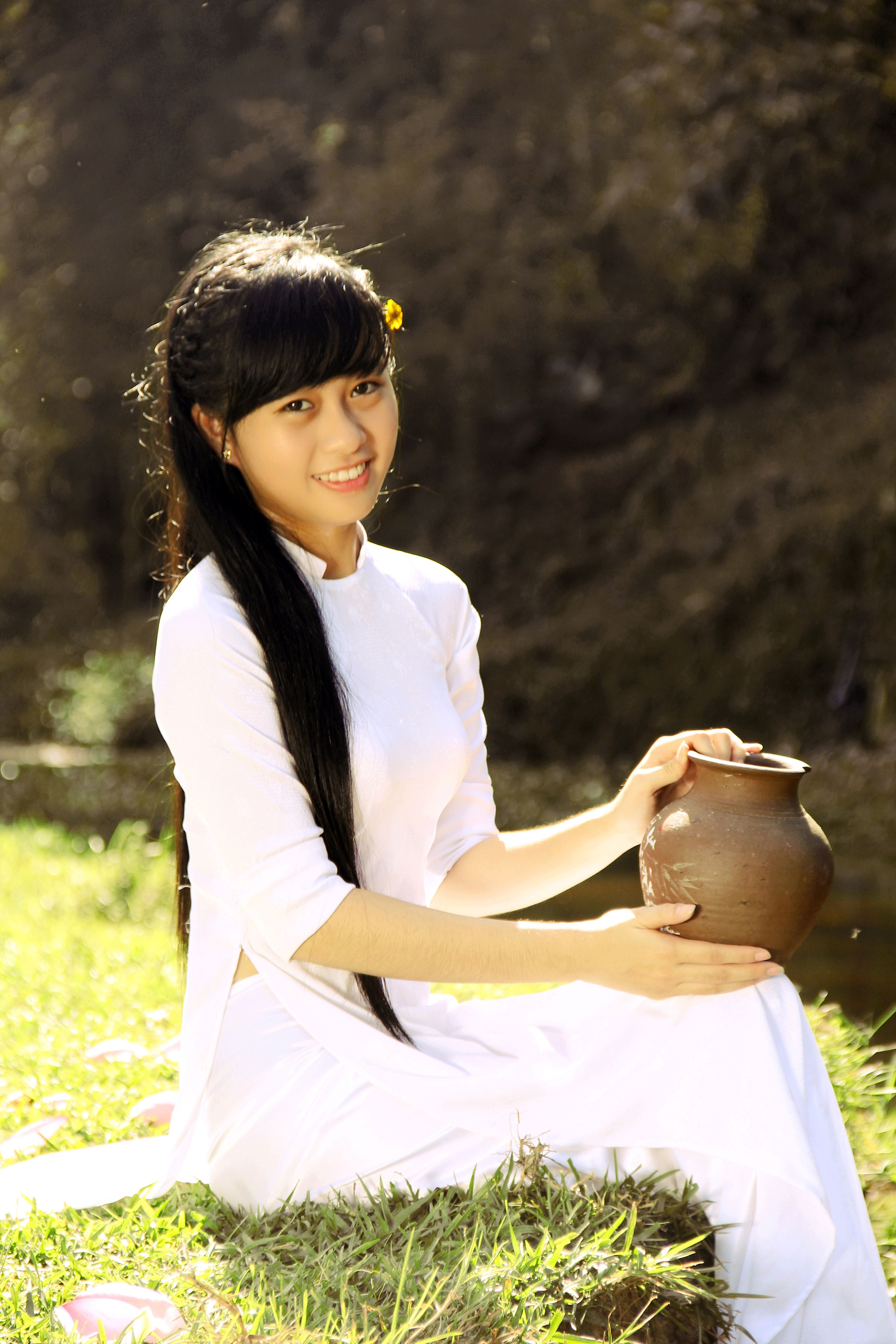 A young woman in a white áo dài sitting outdoors in Hội An.