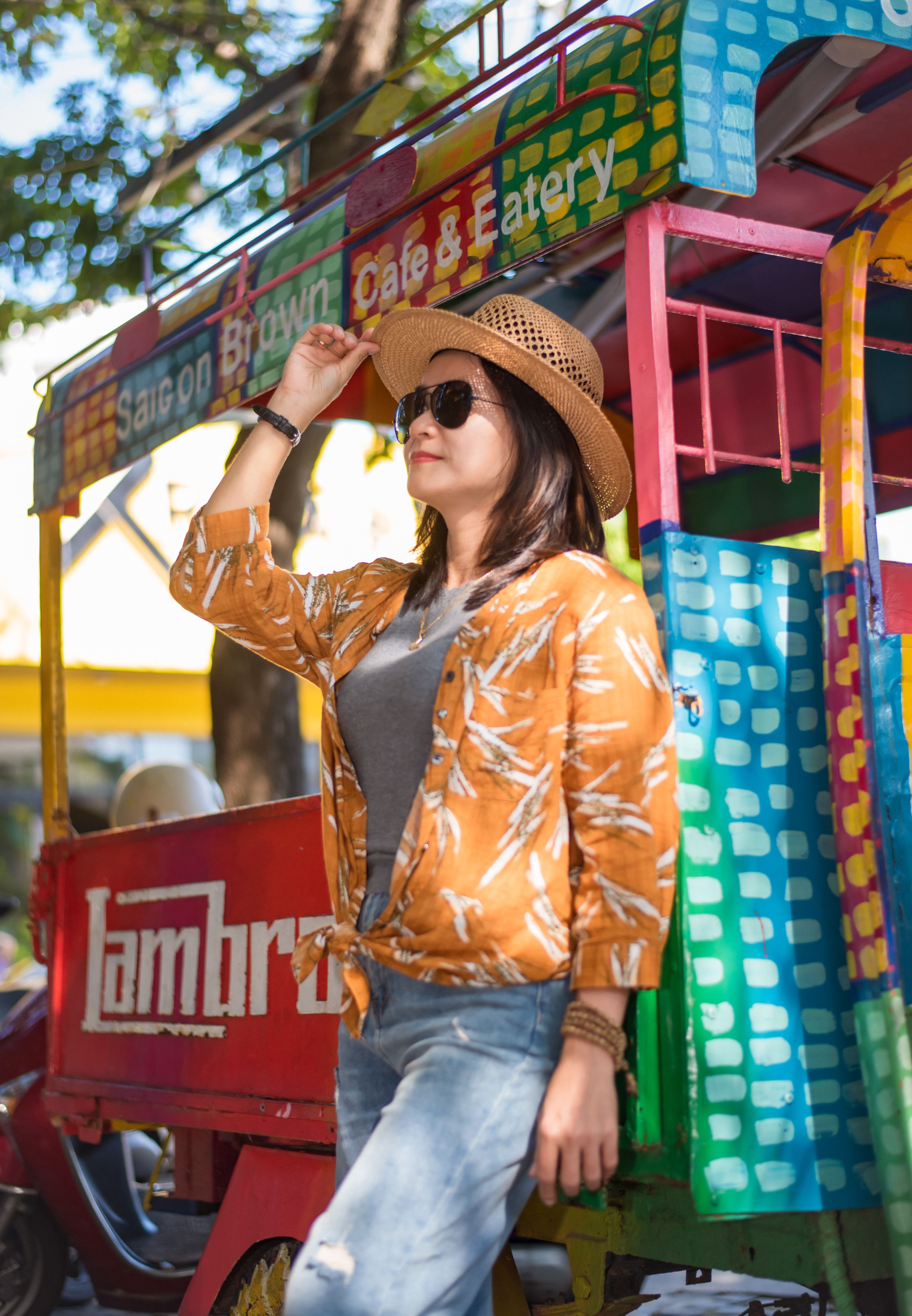Fashionable woman in hat and sunglasses enjoying sunny day by vibrant tricycle.