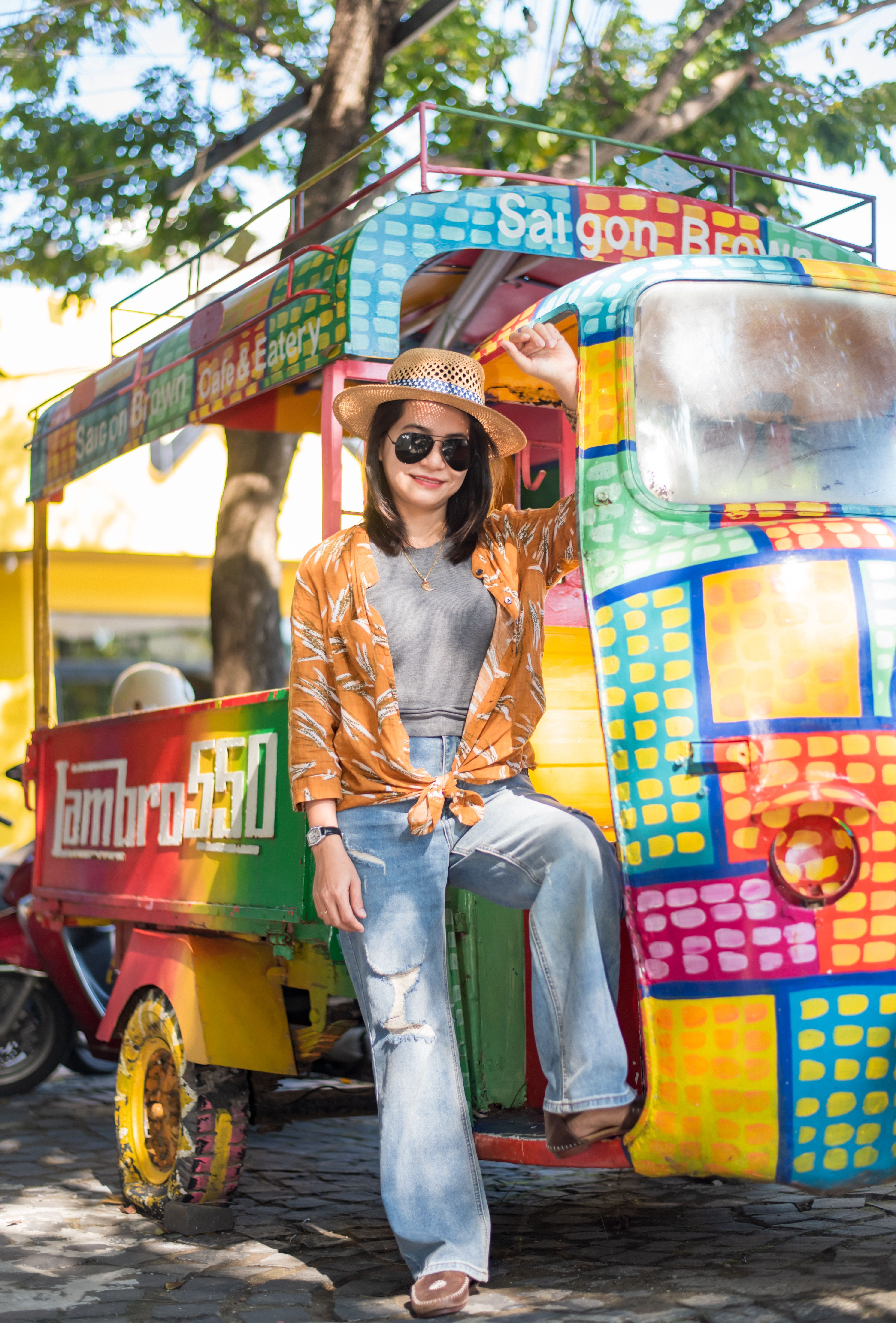 Trendy woman in casual attire poses with vibrant tuk-tuk on a sunny day.