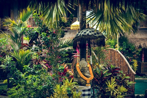 Statue With Orange Necklace Surrounded by Plants and Trees