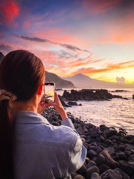 A woman photographs a stunning sunset over the ocean in Tenerife, Canary Islands.