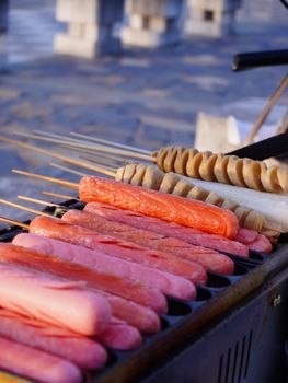 A variety of grilled sausages and skewers on an outdoor street vendor grill.