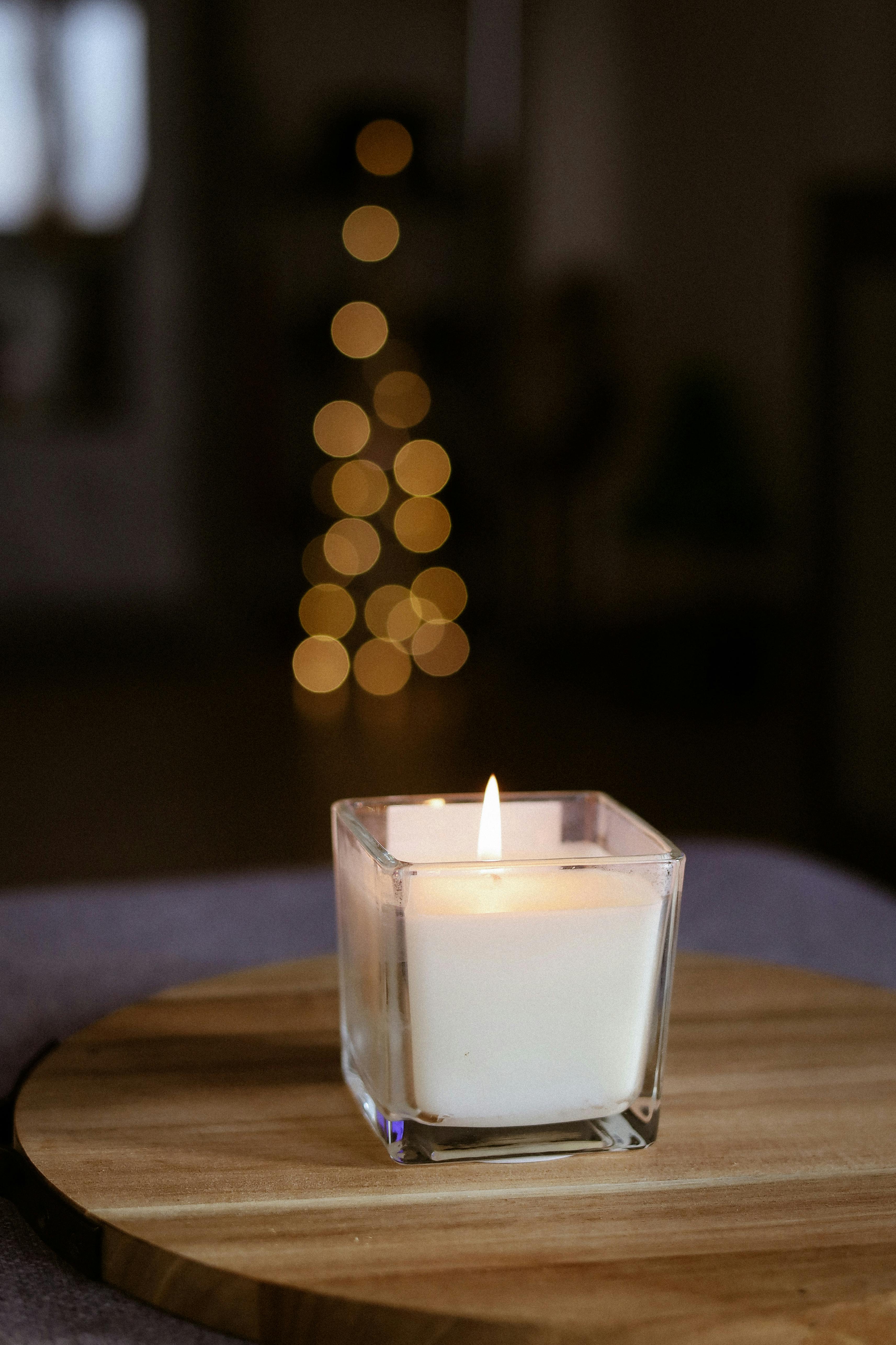 Softly lit candle on wooden surface with festive bokeh lights in the background.