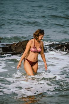 A woman in a bikini enjoying the waves at Anjuna Beach, Goa, India.