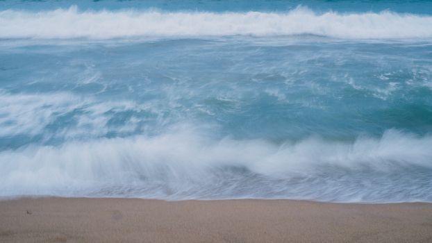 Serene long exposure of waves gently crashing on a sandy beach.