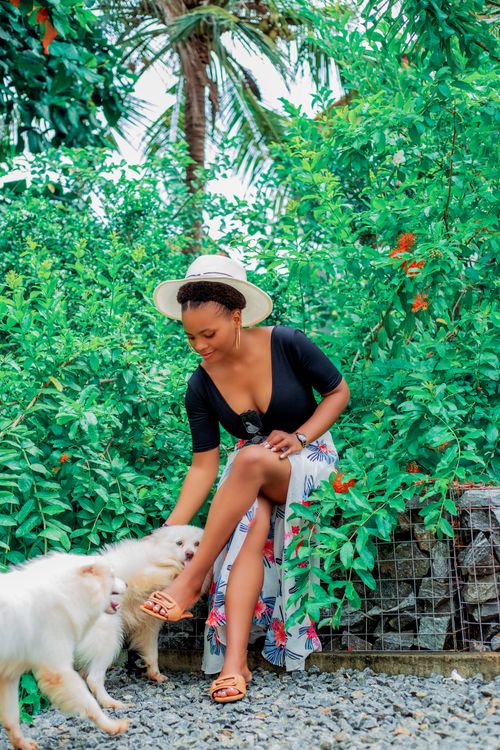 Free Smiling woman in hat playing with dogs amidst lush greenery. Summer vibes. Stock Photo