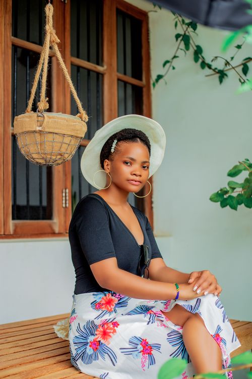 Free Young woman sitting outdoors with a stylish look in a sun hat and floral skirt. Stock Photo