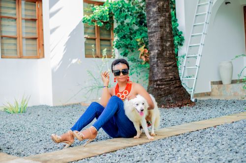 Free Fashionable woman sitting with her dog in a sunny outdoor setting, exuding style and elegance. Stock Photo