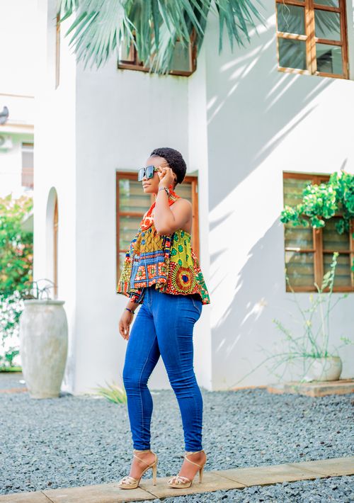 Free A fashionable woman wearing an African print top and jeans standing outdoors. Stock Photo