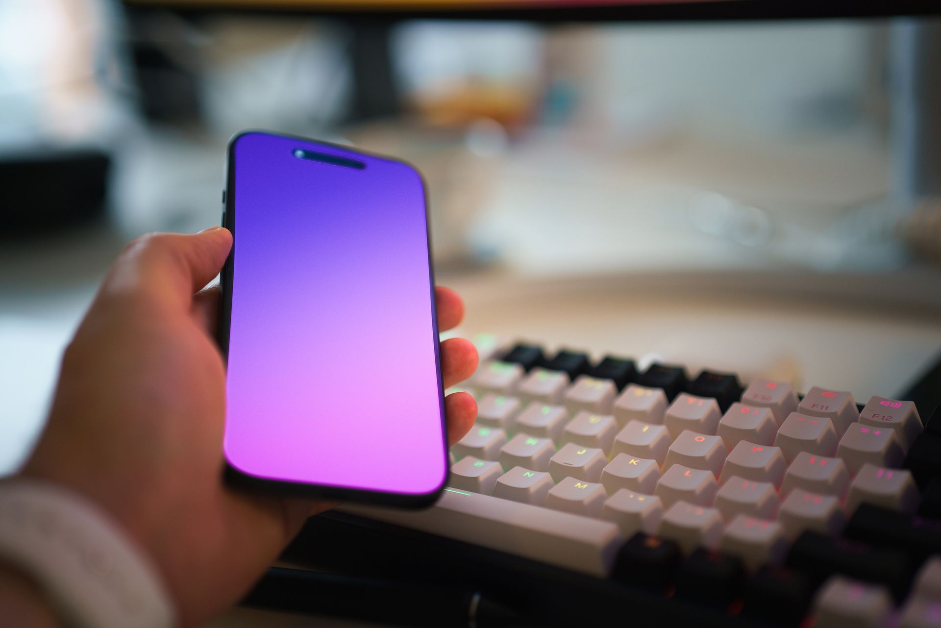 Hand holding blank screen colour gradient smartphone computer keyboard