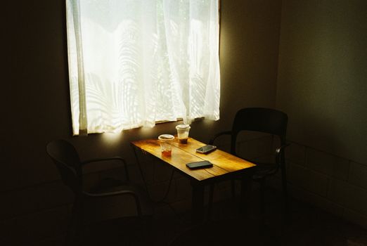 A warm, inviting coffee table setup with drinks, illuminated by soft natural light through a window curtain.