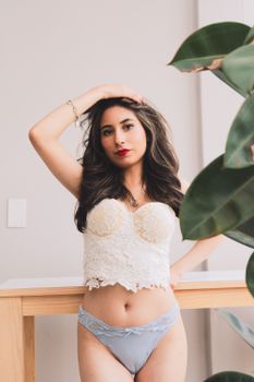 Stylish indoor portrait of a woman in lace lingerie with a plant.