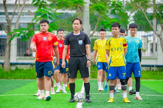 Soccer players and referee prepare for a match on a green field in Hà Nội.