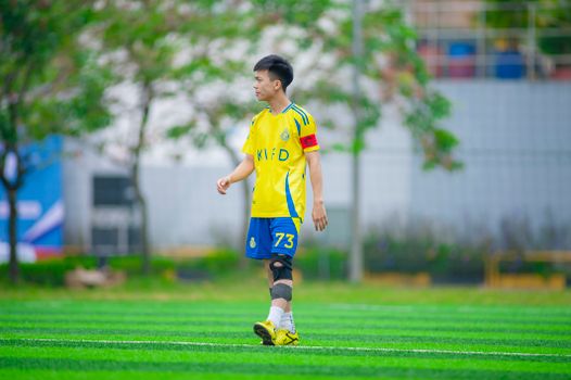 A young soccer player on the field wearing a yellow jersey in Hà Nội, Việt Nam.