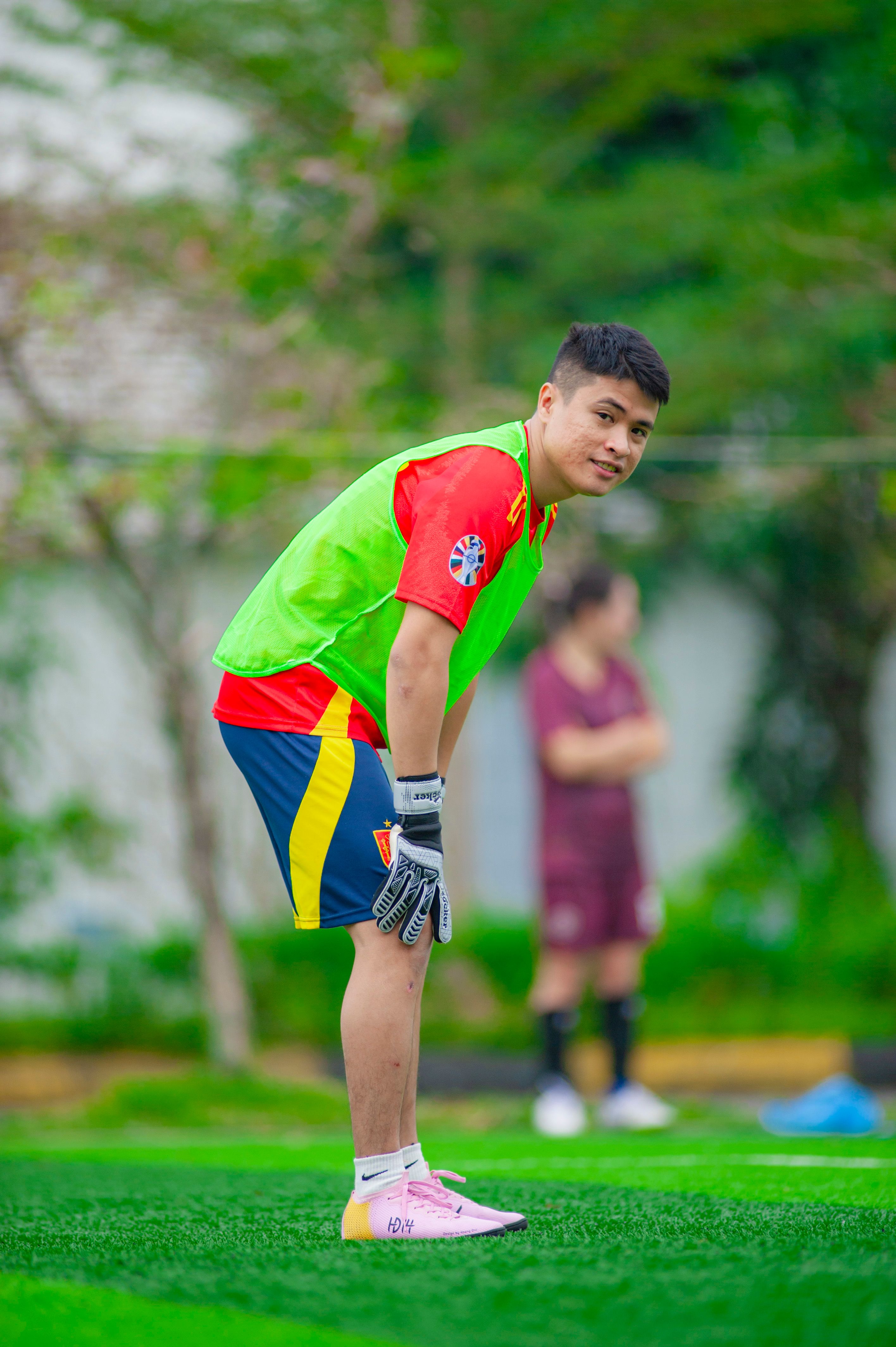 A young goalkeeper bends, focusing during a soccer training match outdoors.