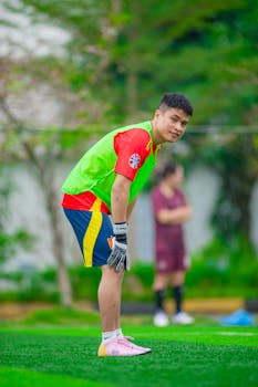 A young goalkeeper bends, focusing during a soccer training match outdoors.