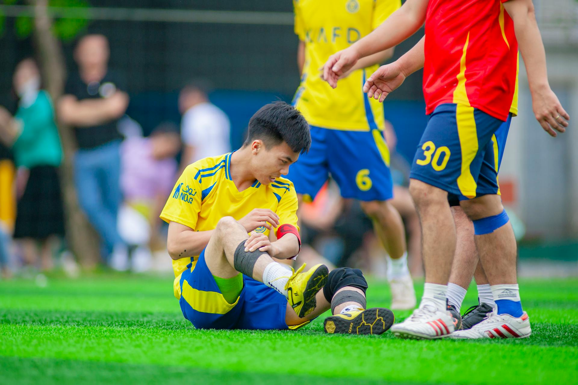 Amateur soccer player sitting on grass, nursing a leg injury during game in Hanoi, Vietnam.