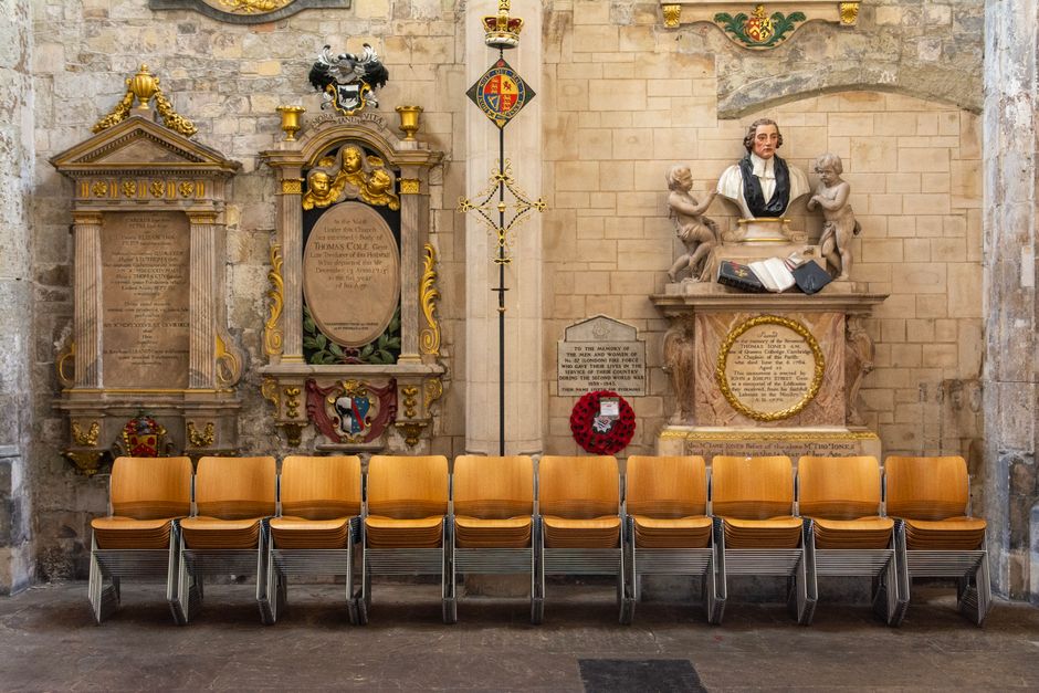 Interior of a historic church featuring memorials and a row of stacked chairs against stone walls.