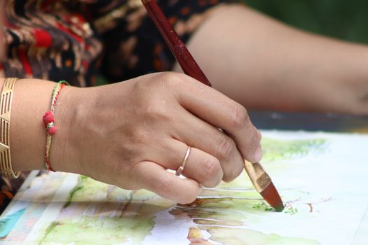 Closeup of a person's hand painting with watercolors on paper.