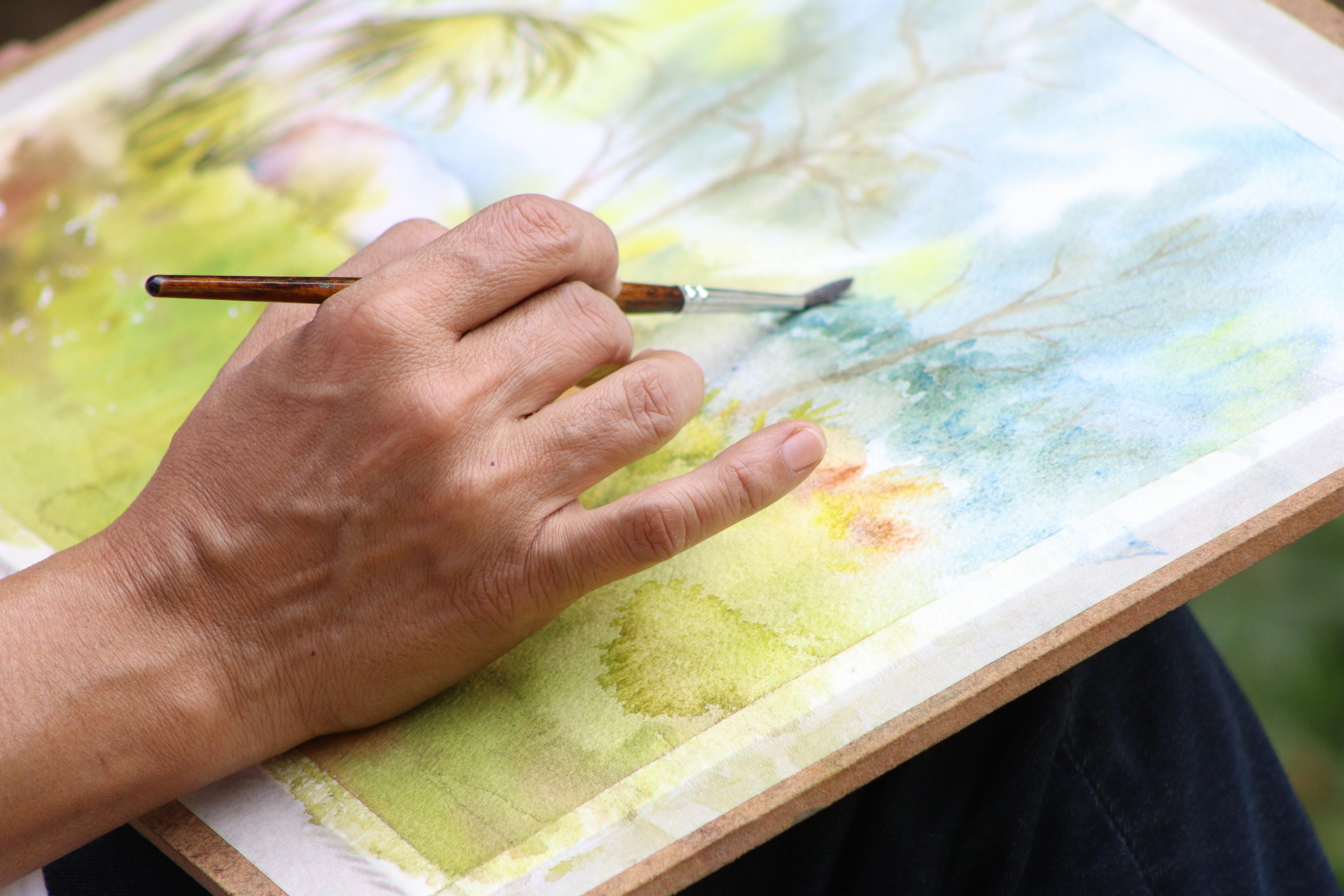 Close-up of an artist painting a watercolor landscape with a brush.