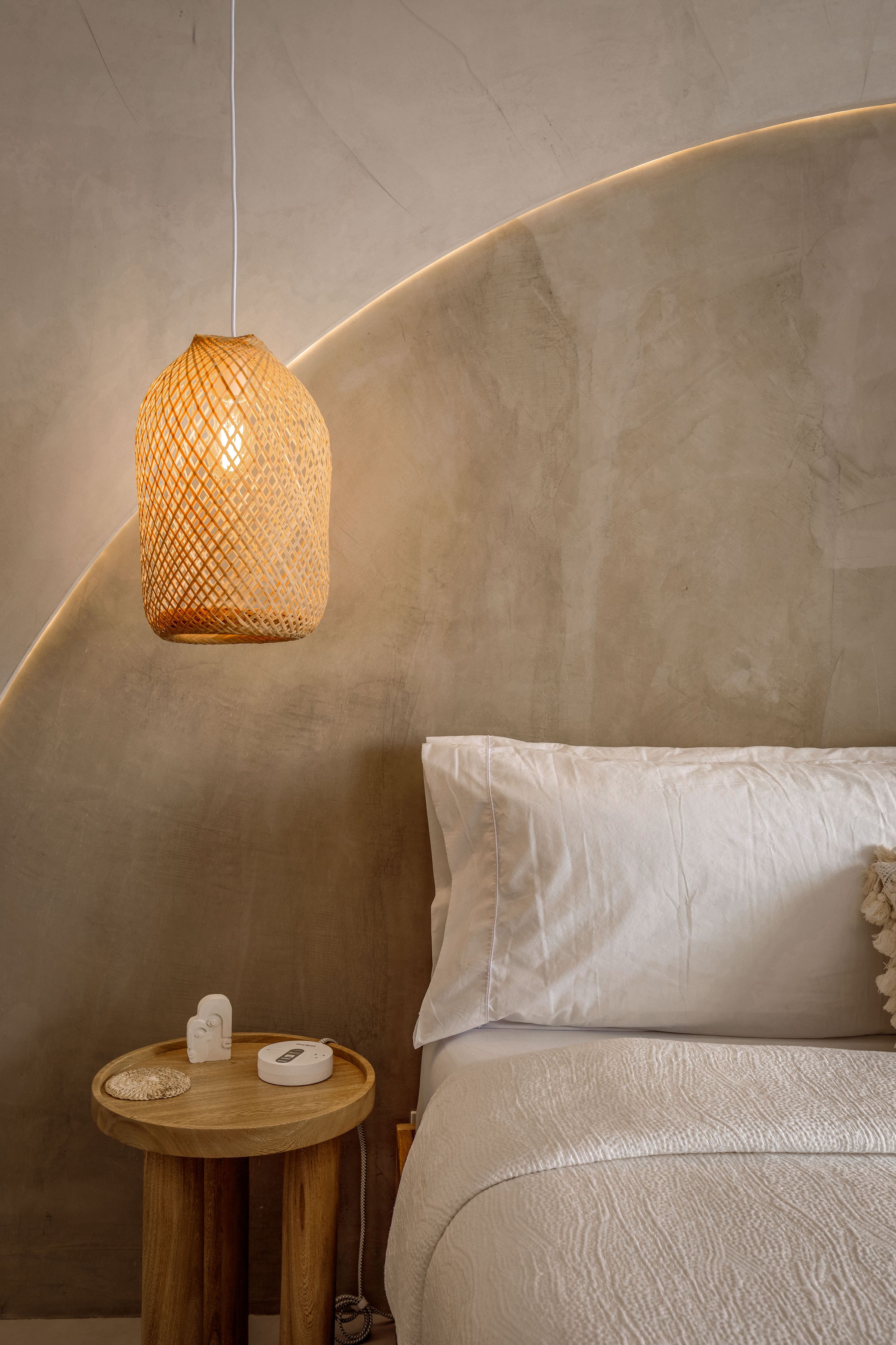 Minimal bedroom with a bed set into a shallow wall recess beneath a woven pendant