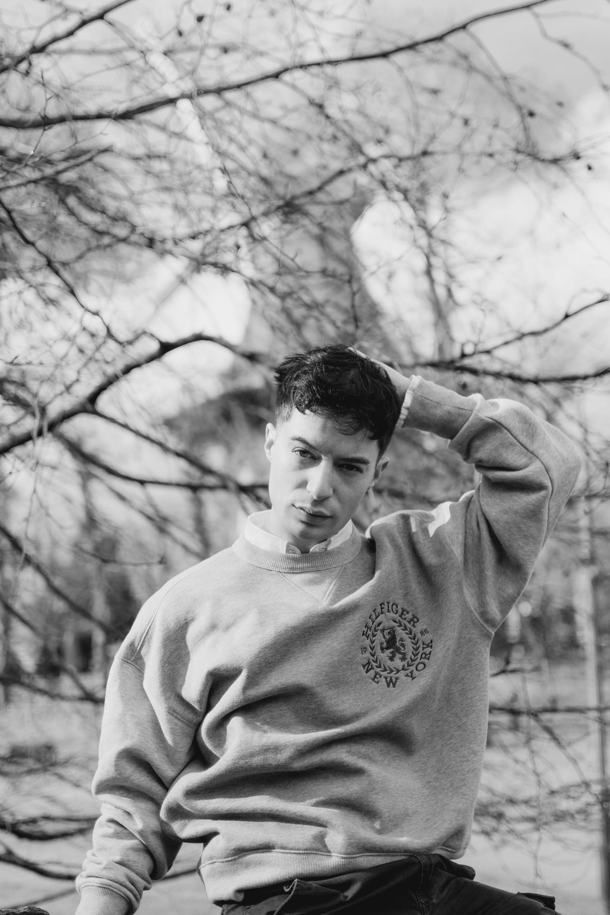 Black and white outdoor portrait of a young man in casual attire posing thoughtfully.
