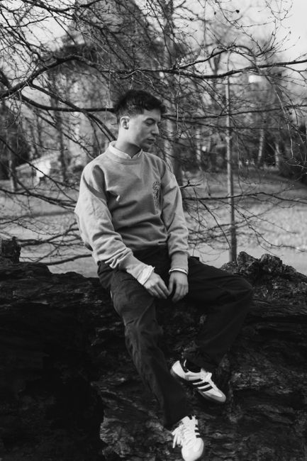Black and white portrait of a man sitting outdoors on a rock in a natural setting.