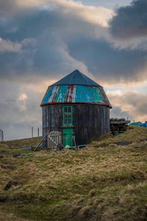 Free A rustic round farmhouse with a weathered roof stands against a dynamic cloudy sky. Stock Photo