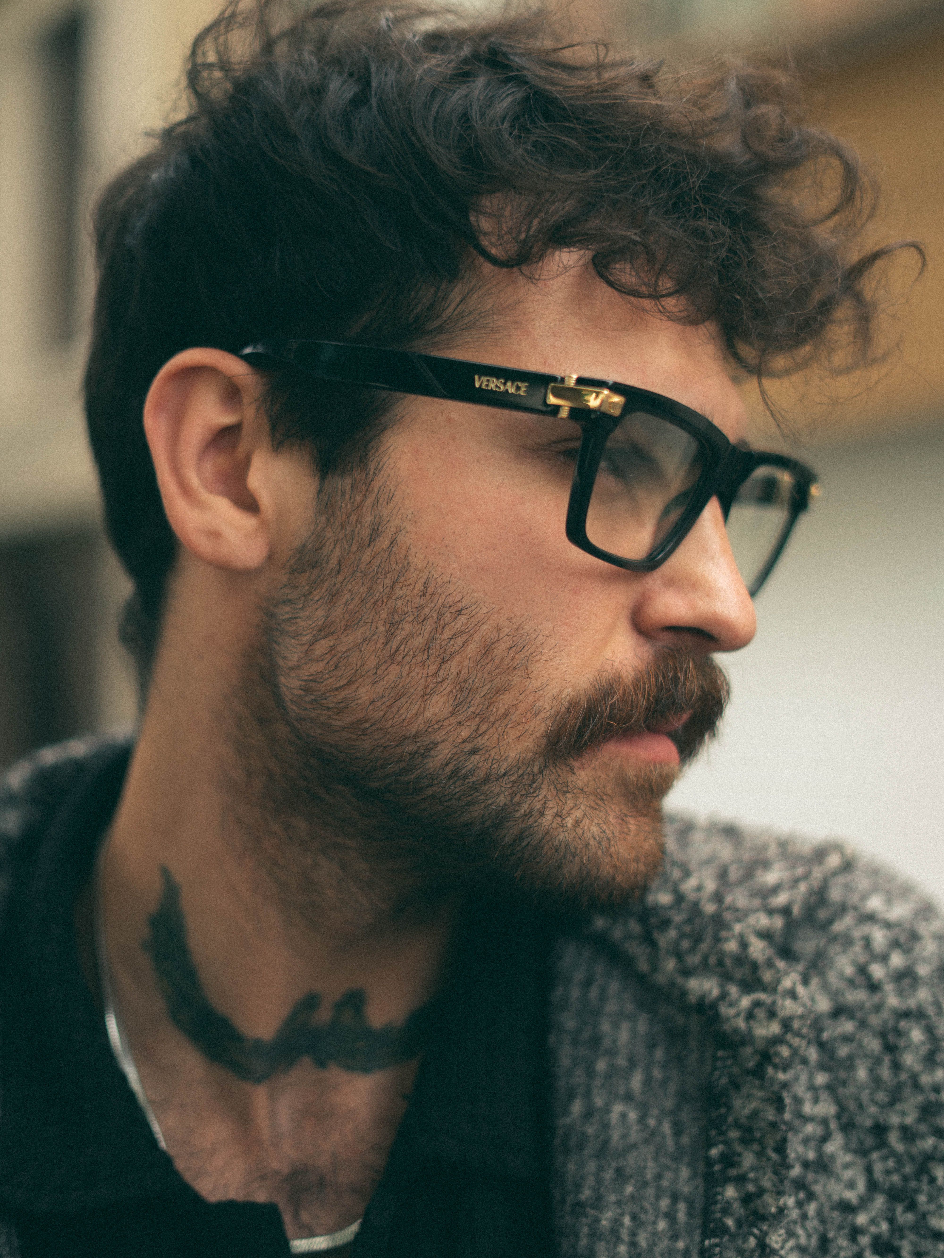 Profile of a stylish man wearing glasses with a tattoo on neck.