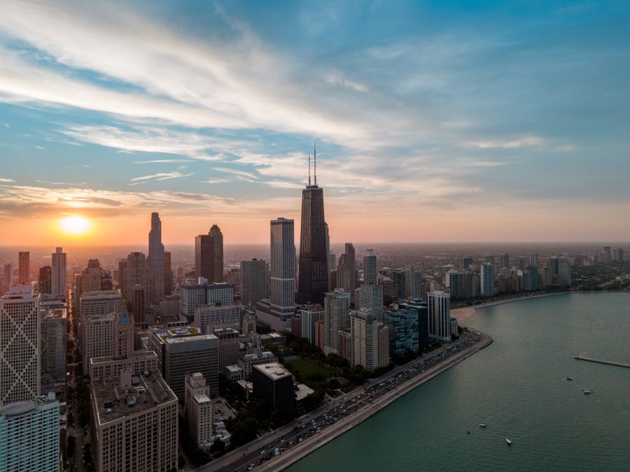 Golden hour sunset over Chicago's downtown skyline dominated by Willis Tower, with Lake Michigan and curved shoreline visible