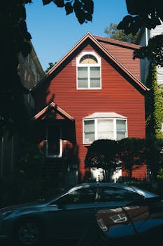 A cozy red house with trees casting shadows, perfect for urban living.