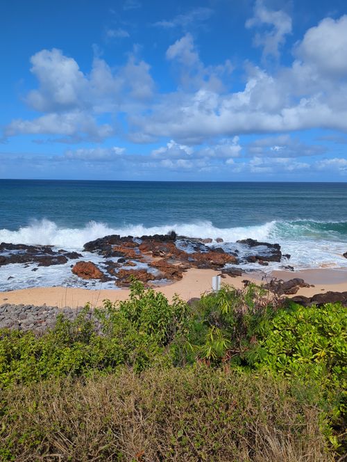 Free A beautiful rocky beach with ocean waves crashing under a clear blue sky, offering a tranquil escape. Stock Photo