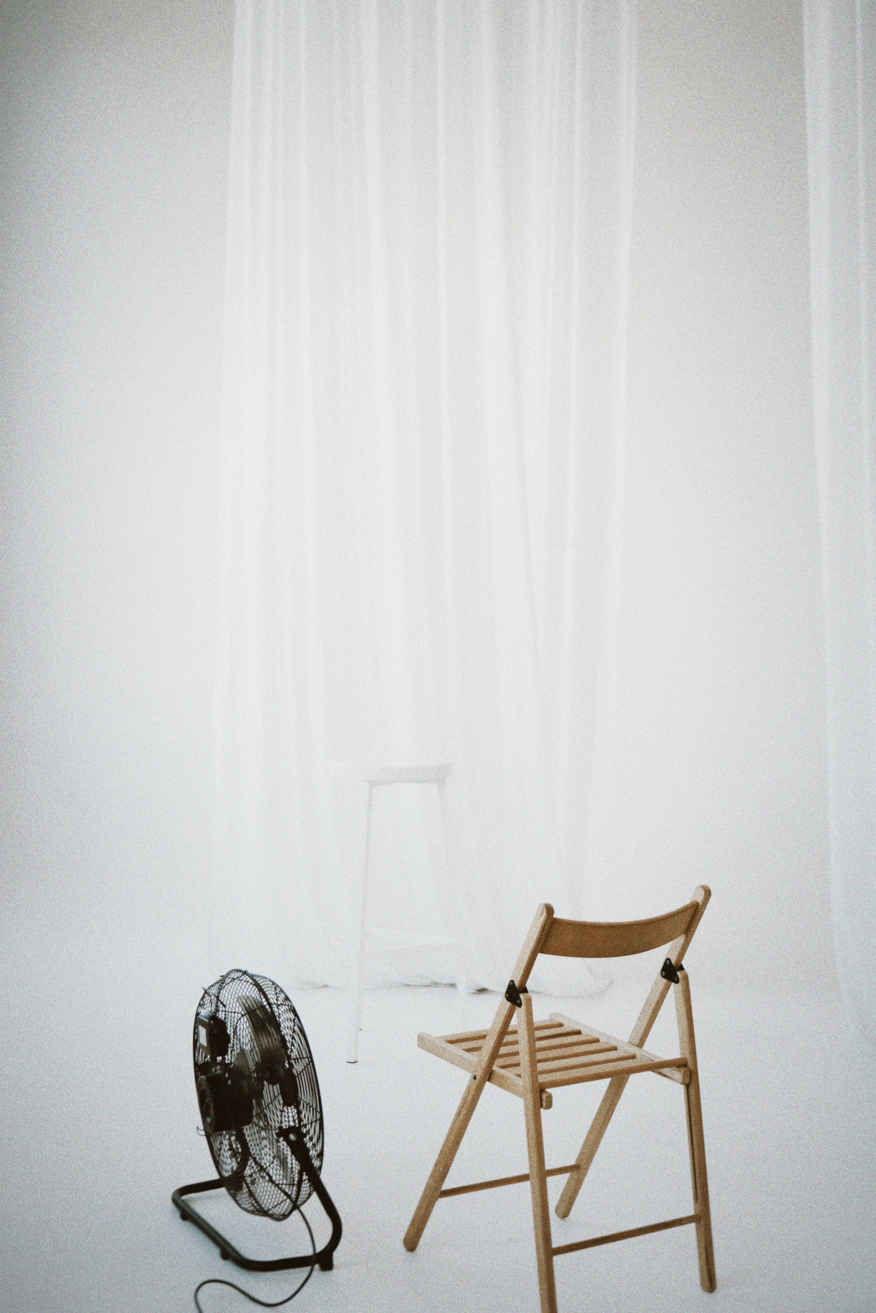 A minimalist setup with a wooden chair and fan against a white backdrop, perfect for design concepts.