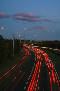 Long exposure of cars on a highway at twilight, showcasing bright red light trails.