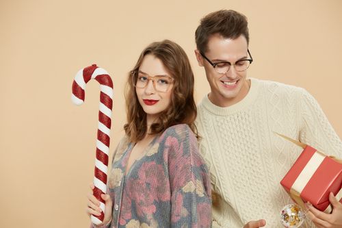 Free A cheerful couple wearing glasses and holding a candy cane and gift, celebrating Christmas. Stock Photo