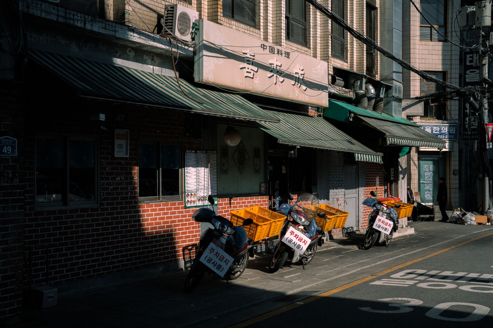 Urban street view in Seoul featuring motorbikes outside a local restaurant.