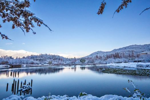 A tranquil lake scene in Seoul dusted with fresh snow under a clear blue sky.