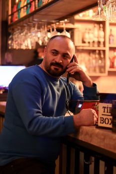 Man in a cozy bar setting talking on the phone next to a tip box.