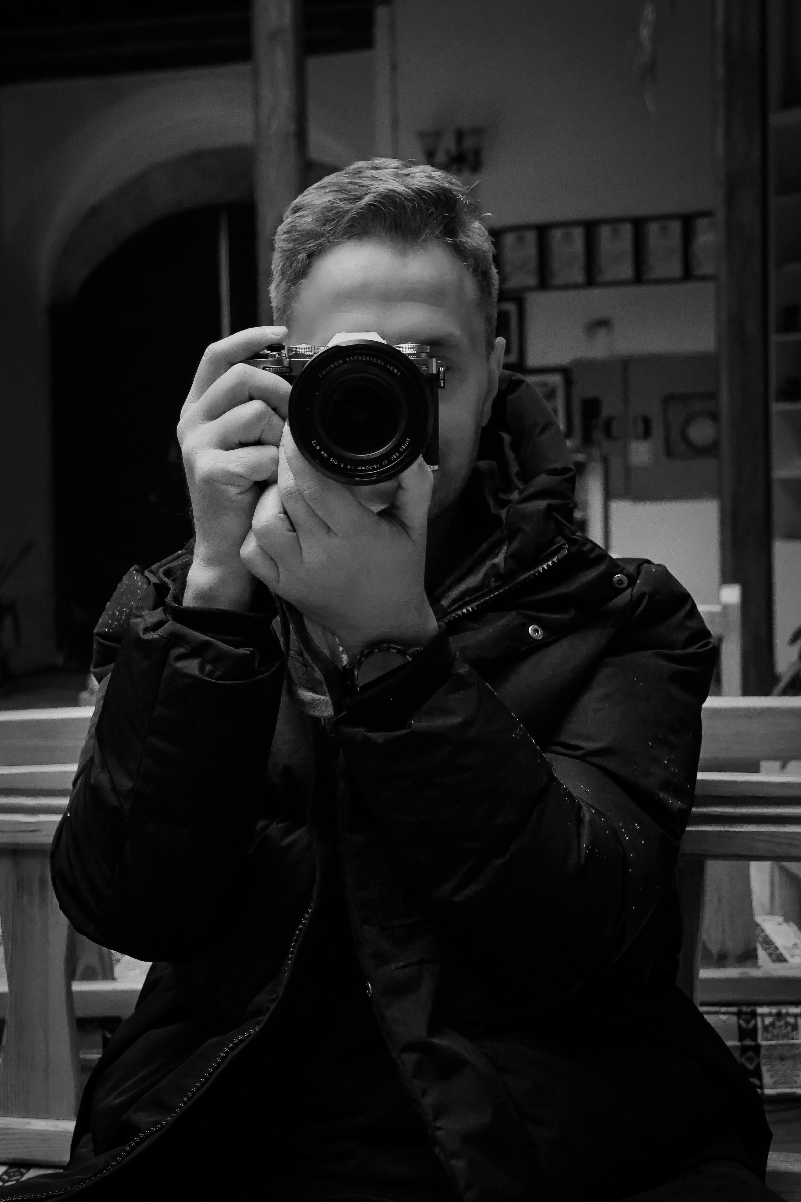 Black and white photo of a person taking a picture indoors.