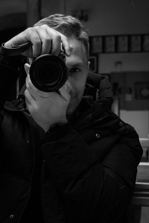 Free Monochrome photo capturing a photographer aiming the camera indoors. Stock Photo