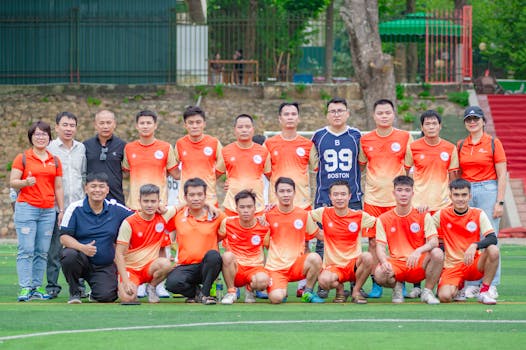 A soccer team poses outdoors in Hanoi, Vietnam, wearing orange uniforms.
