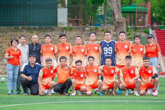 Outdoor group photo of a Vietnamese soccer team in orange uniforms at a park in Hanoi.
