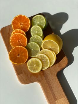 Variety of citrus slices on a wooden board with sunlight casting a shadow.