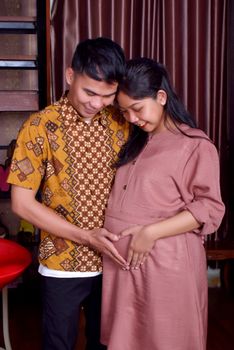 Happy couple celebrating pregnancy, forming a heart shape on belly. - Fotografer Sidoarjo