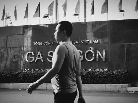 Black and white street scene with a man walking past Saigon Railway Station in Ho Chi Minh City.